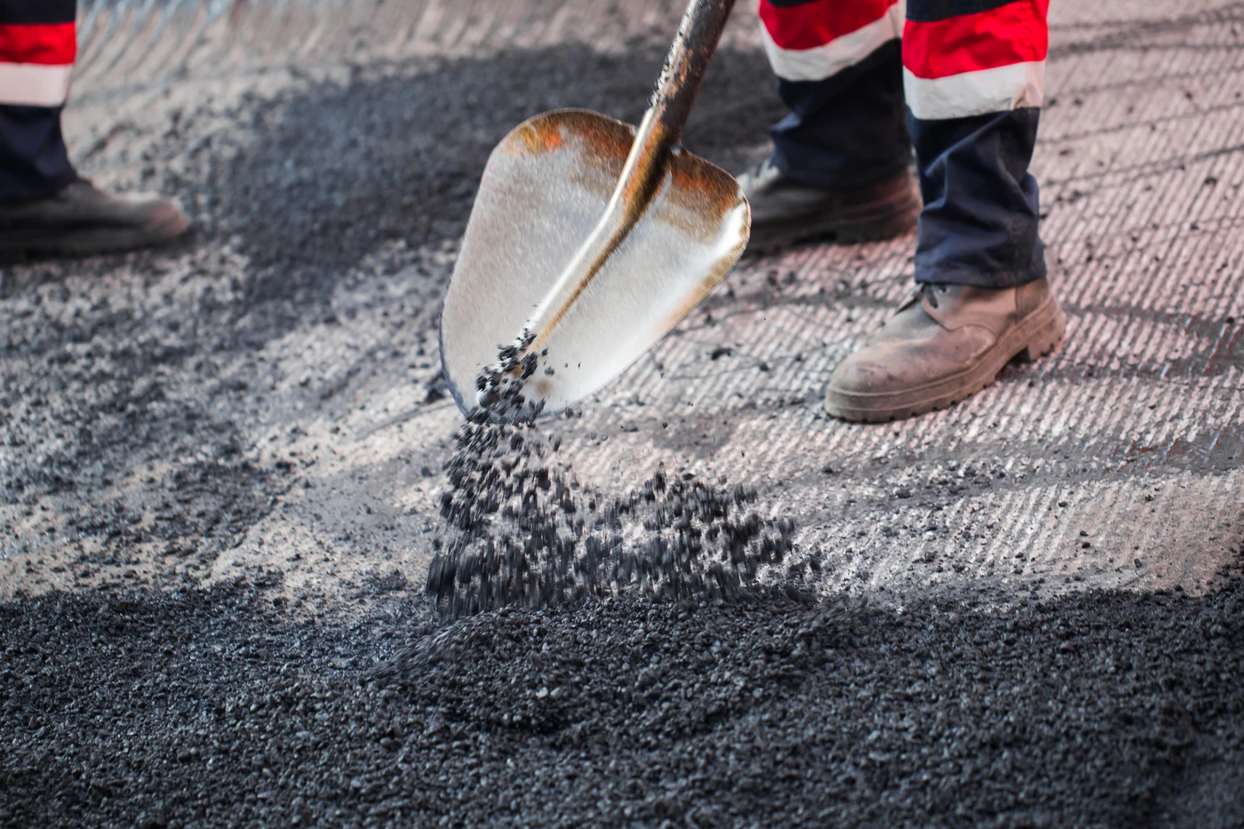 Trabajador extendiendo asfalto con pala durante obra vial de empresa de construcción en Málaga y la Costa del Sol